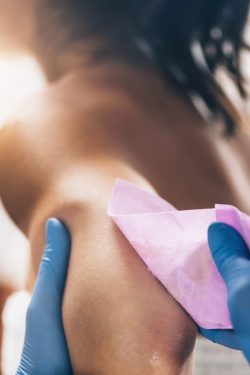 Waxing arms. Beautician removing unwanted hair from female arm with wax strips in a beauty salon.